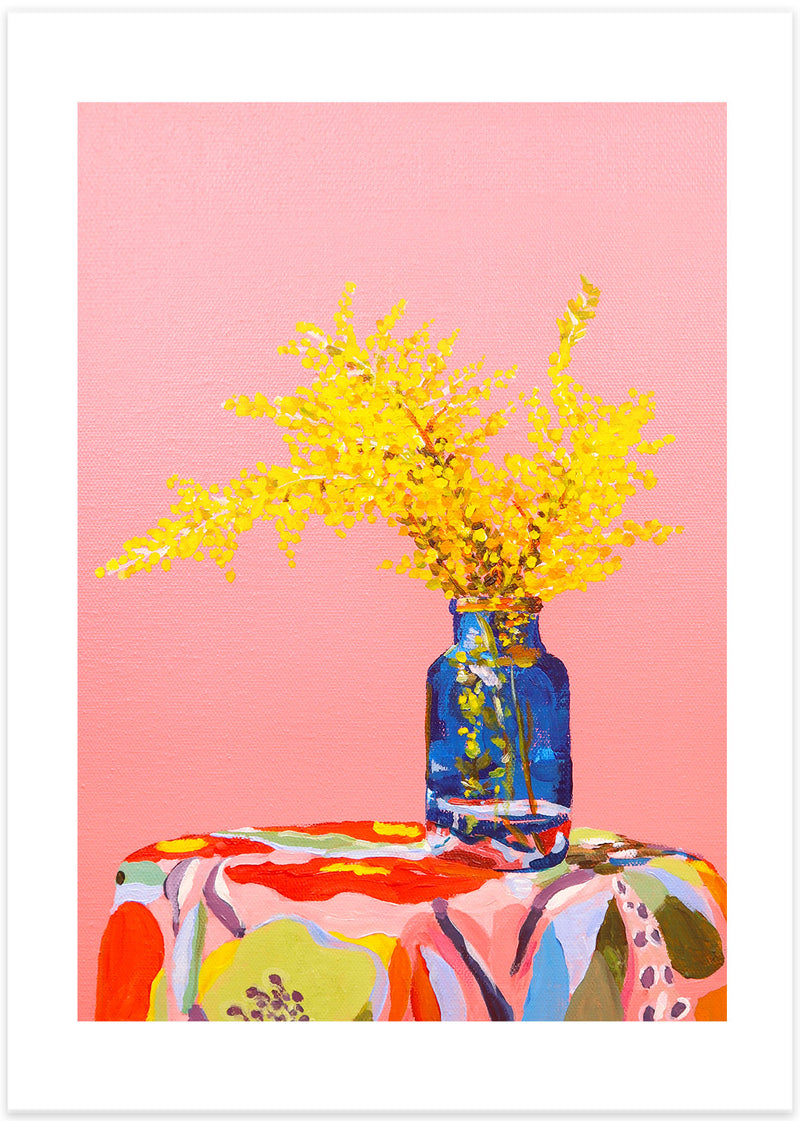 Poster med målning av gula blommor i en blå glasvas ståendes på ett bord med en färgstark blommig duk mot en rosa bakgrund.